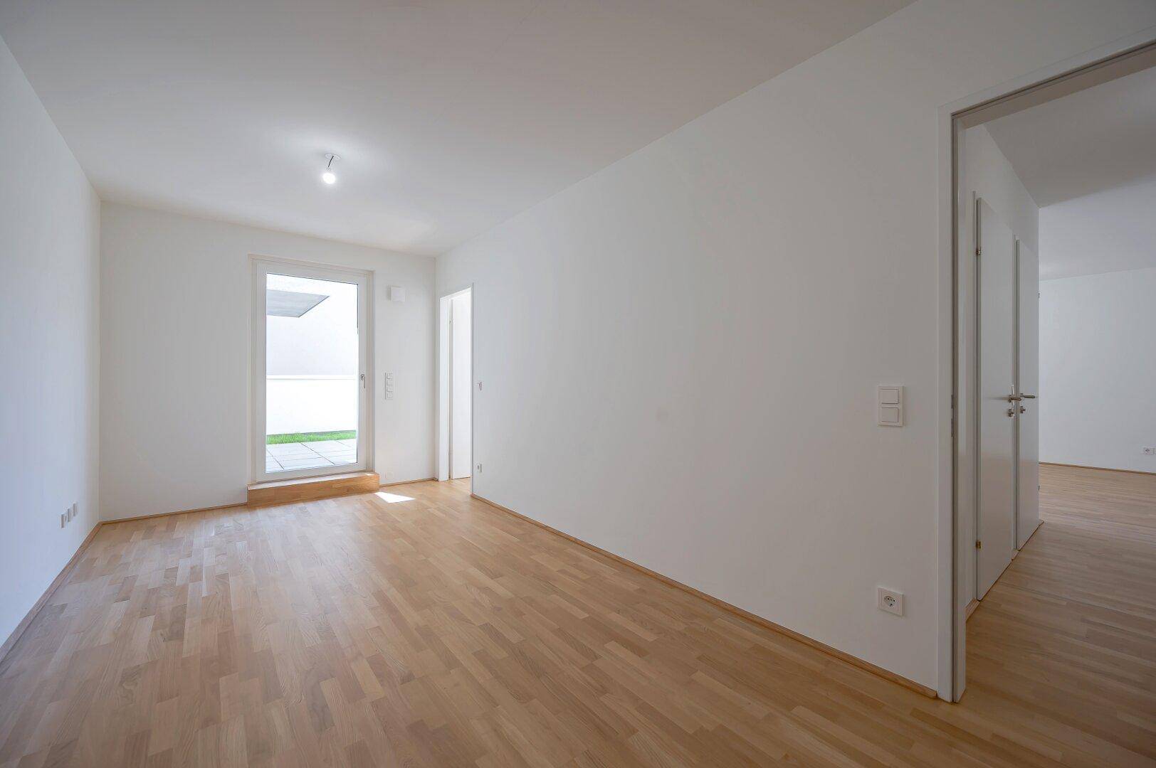 Heller Raum mit Holzboden und Zugang zu einem Außenbereich, ideal für ein Schlafzimmer.