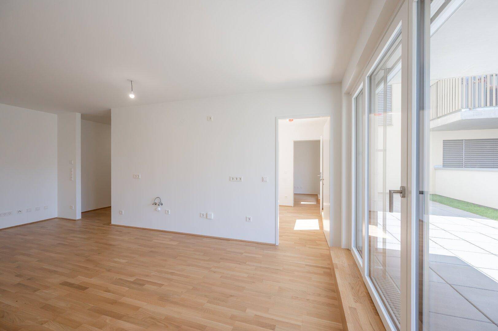 Helles, leeres Wohnzimmer mit Parkettboden und Zugang zur Terrasse.
