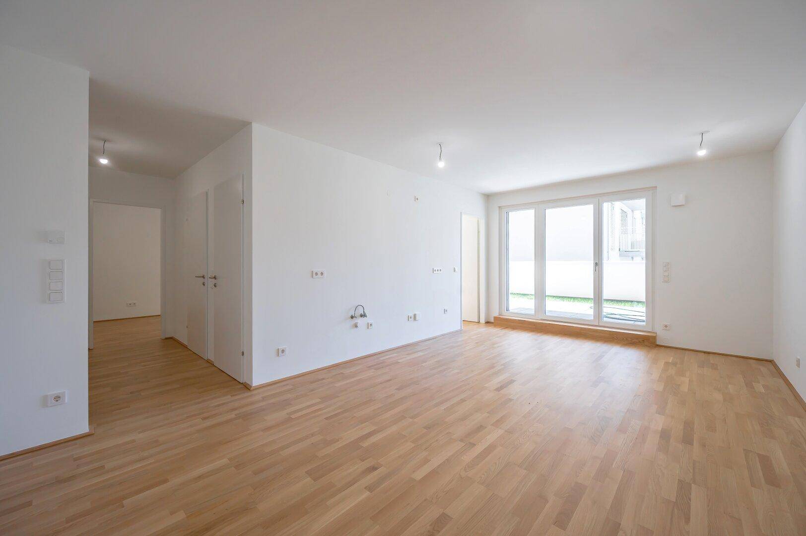 Lichtdurchfluteter Wohnbereich mit Holzboden und großen Fenstern, bereit zur individuellen Gestaltung.