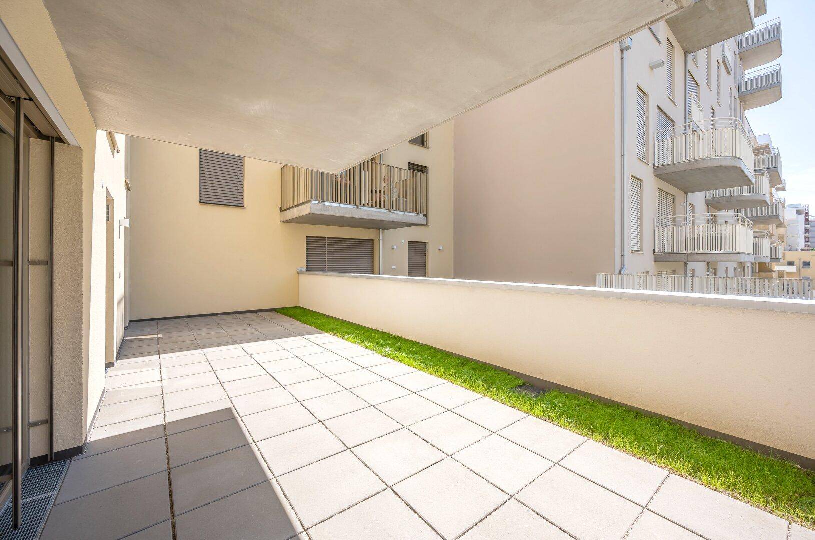 Weitläufige Terrasse mit Grünfläche und Blick auf die moderne Architektur des Gebäudes.