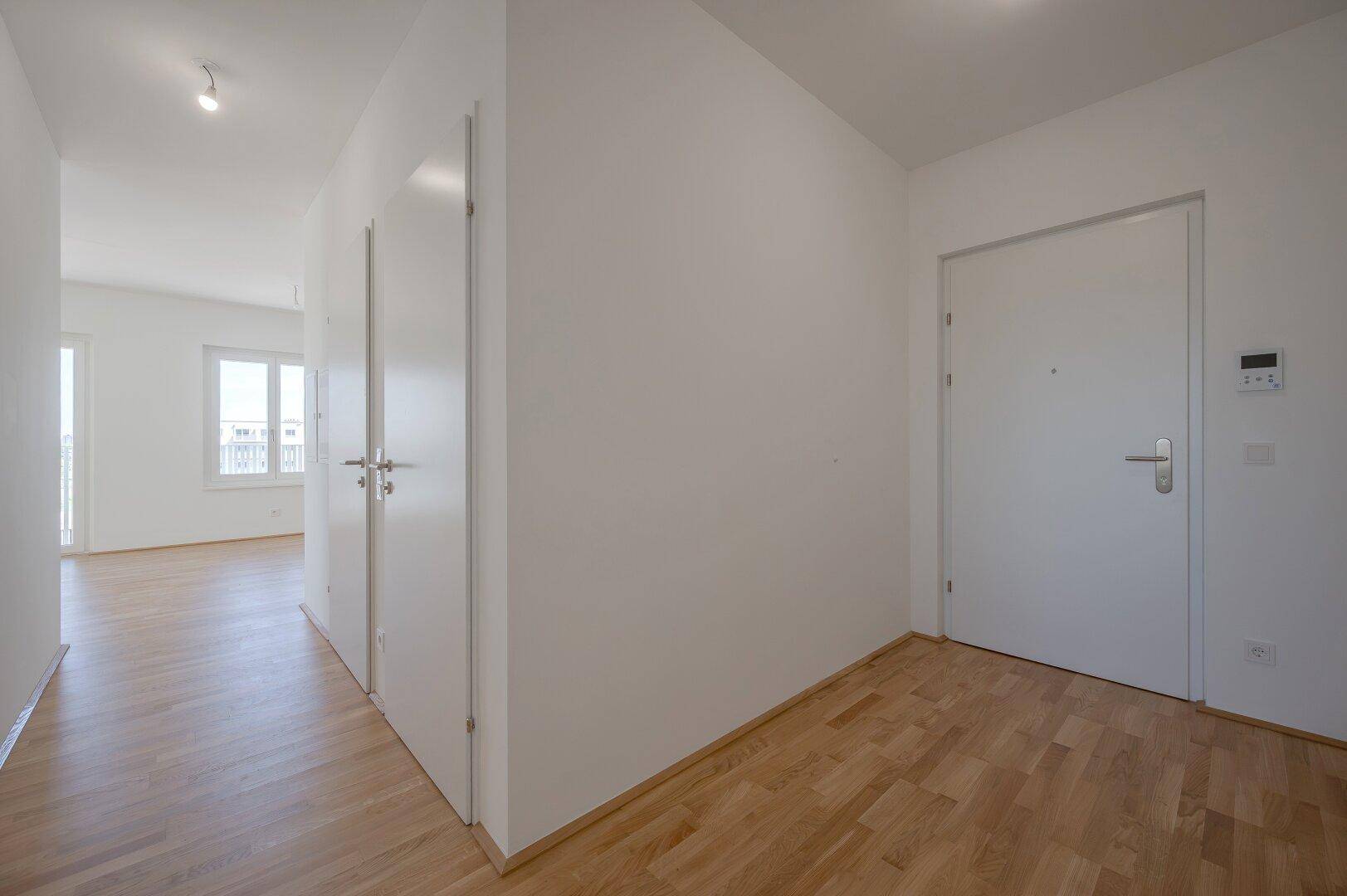 Heller Eingangsbereich mit Holzboden und modernen weißen Türen in einem Neubau.