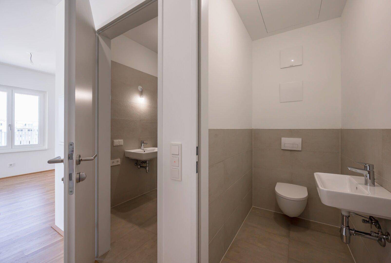 Modernes Gäste-WC mit beigefarbenen Fliesen, wandhängendem WC und kleinem Waschbecken.