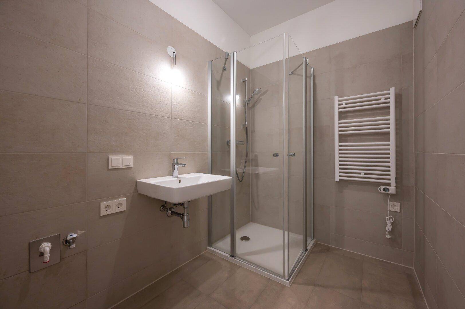 Geräumiges Badezimmer mit modernen Fliesen, Duschkabine und praktischem Waschbecken.
