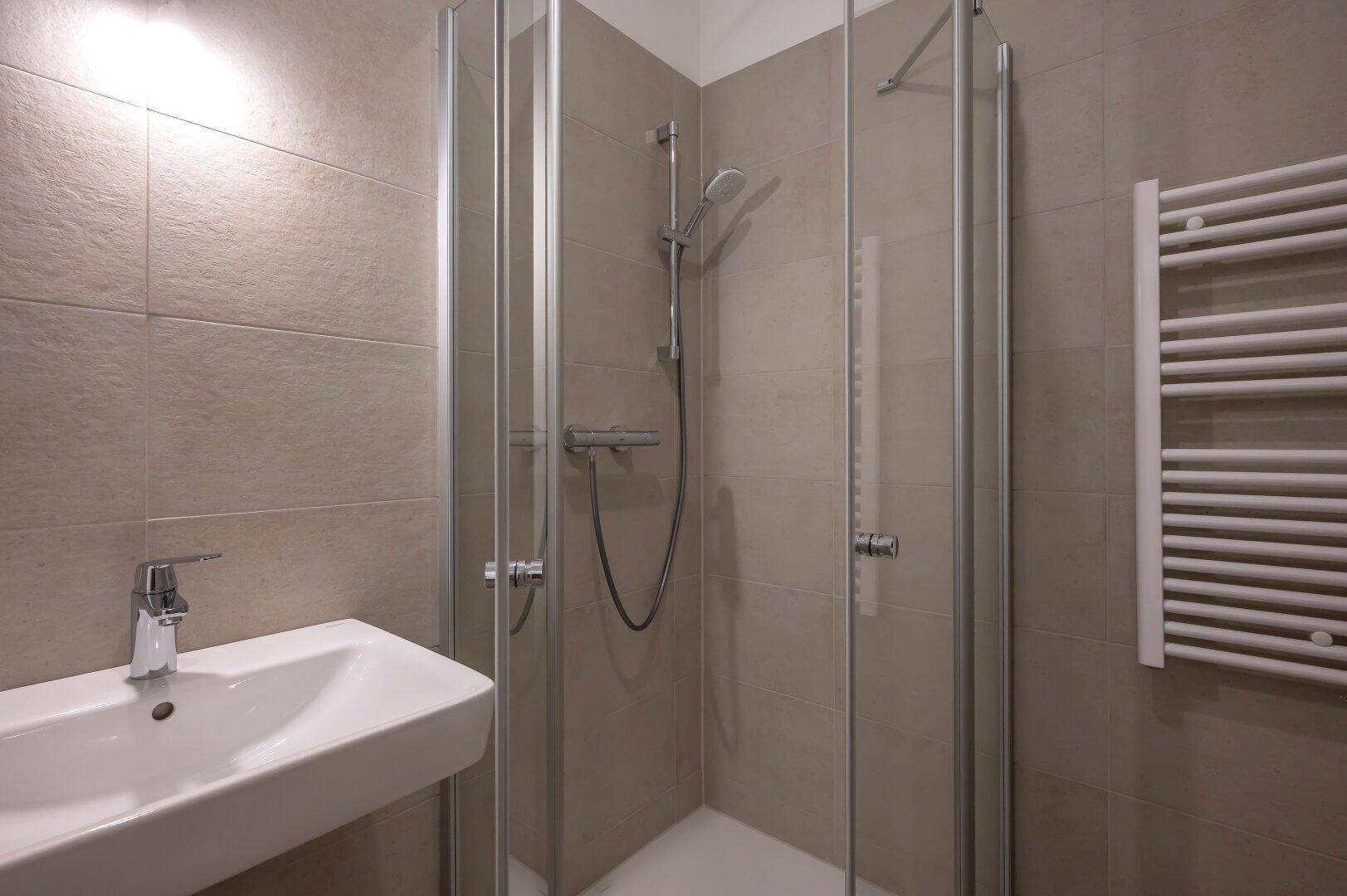 Modernes Badezimmer mit beigefarbenen Fliesen, Duschkabine und beheiztem Handtuchhalter.