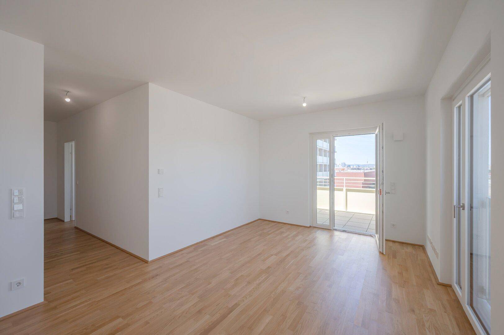 Großes, helles Wohnzimmer mit Parkettboden und Zugang zu einer sonnigen Terrasse.