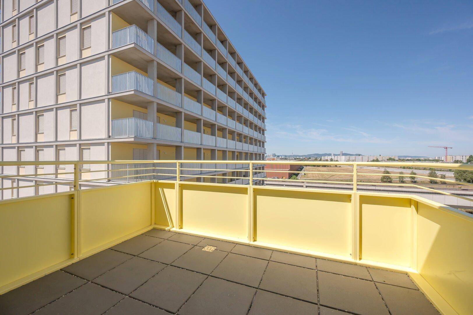Heller Balkon mit gelbem Geländer und Fliesenboden, bietet weiten Blick über die Umgebung.