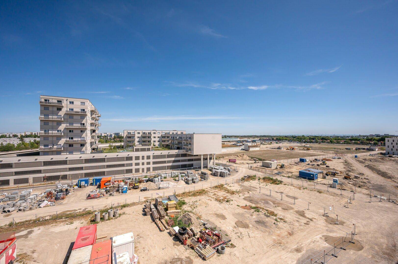 Panoramablick über eine Baustelle mit neuen Gebäuden und weitem Horizont unter blauem Himmel.