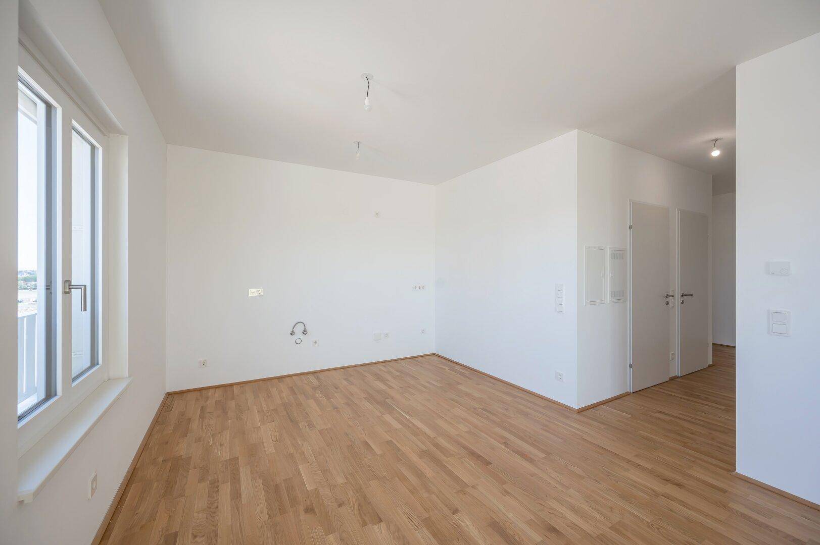 Leeres, helles Zimmer mit Parkettboden und großem Fenster, bereit für die Einrichtung.