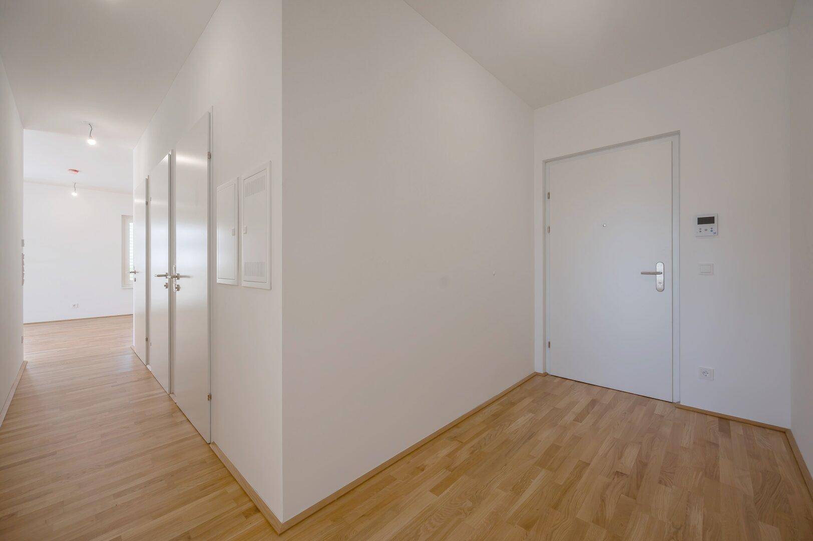 Eingangsbereich mit hellem Holzfußboden und einer modernen weißen Tür, die in die Wohnung führt.