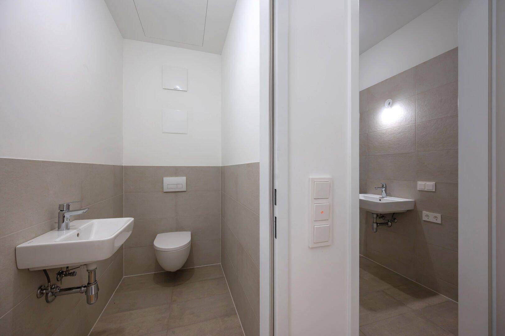 Modernes Gäste-WC mit Wand-WC und Waschbecken, daneben ein weiterer Sanitärbereich.