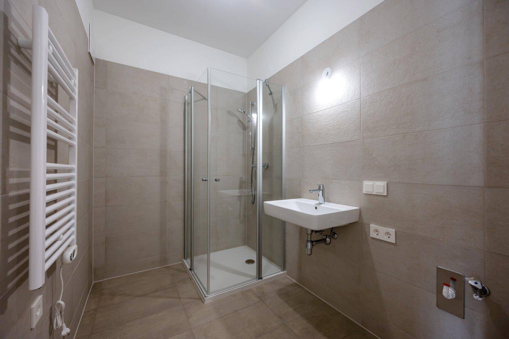 Modernes Badezimmer mit Duschkabine, Waschbecken und beheiztem Handtuchhalter, komplett gefliest.