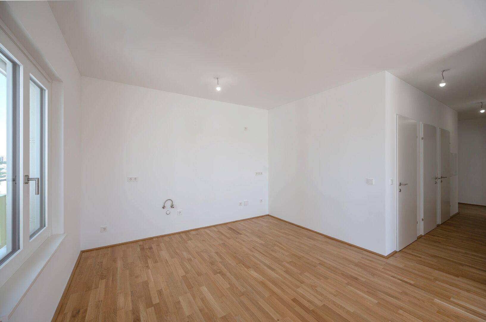 Leerer Raum mit Parkettboden und Fenster, vorbereitet für die Installation einer modernen Küche.