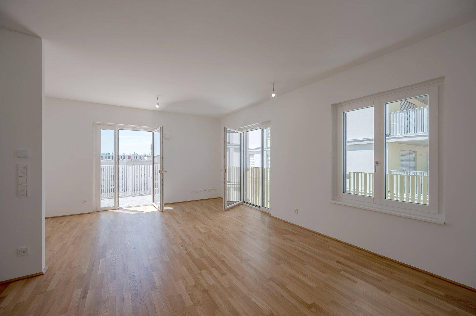Helles, leeres Zimmer mit hellem Parkettboden und Zugang zu einem Balkon, ideal für Wohnzwecke.