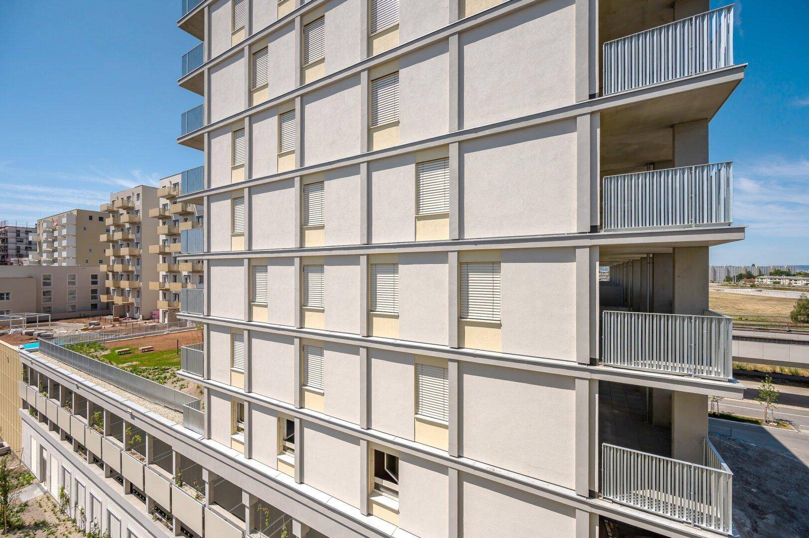 Moderne Fassade eines Wohngebäudes mit zahlreichen Balkonen und Fensterläden unter blauem Himmel.