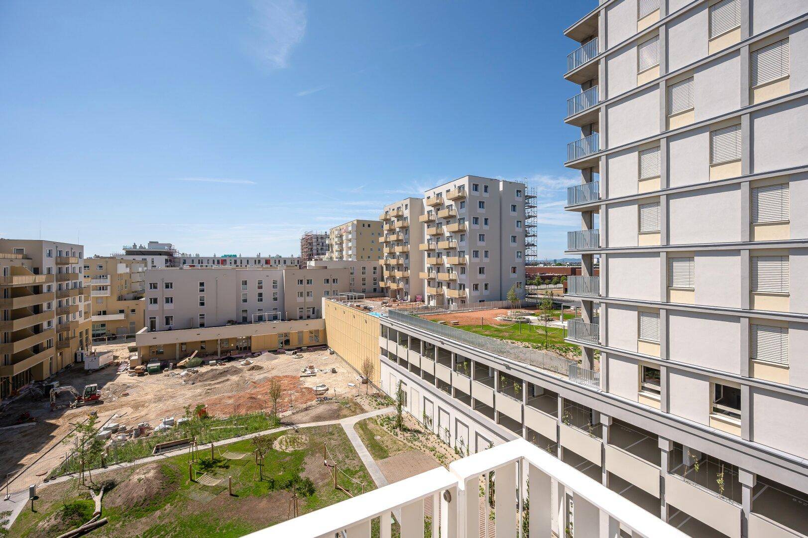 Weitblick von einem Balkon über eine Baustelle, Grünflächen und moderne Wohngebäude.