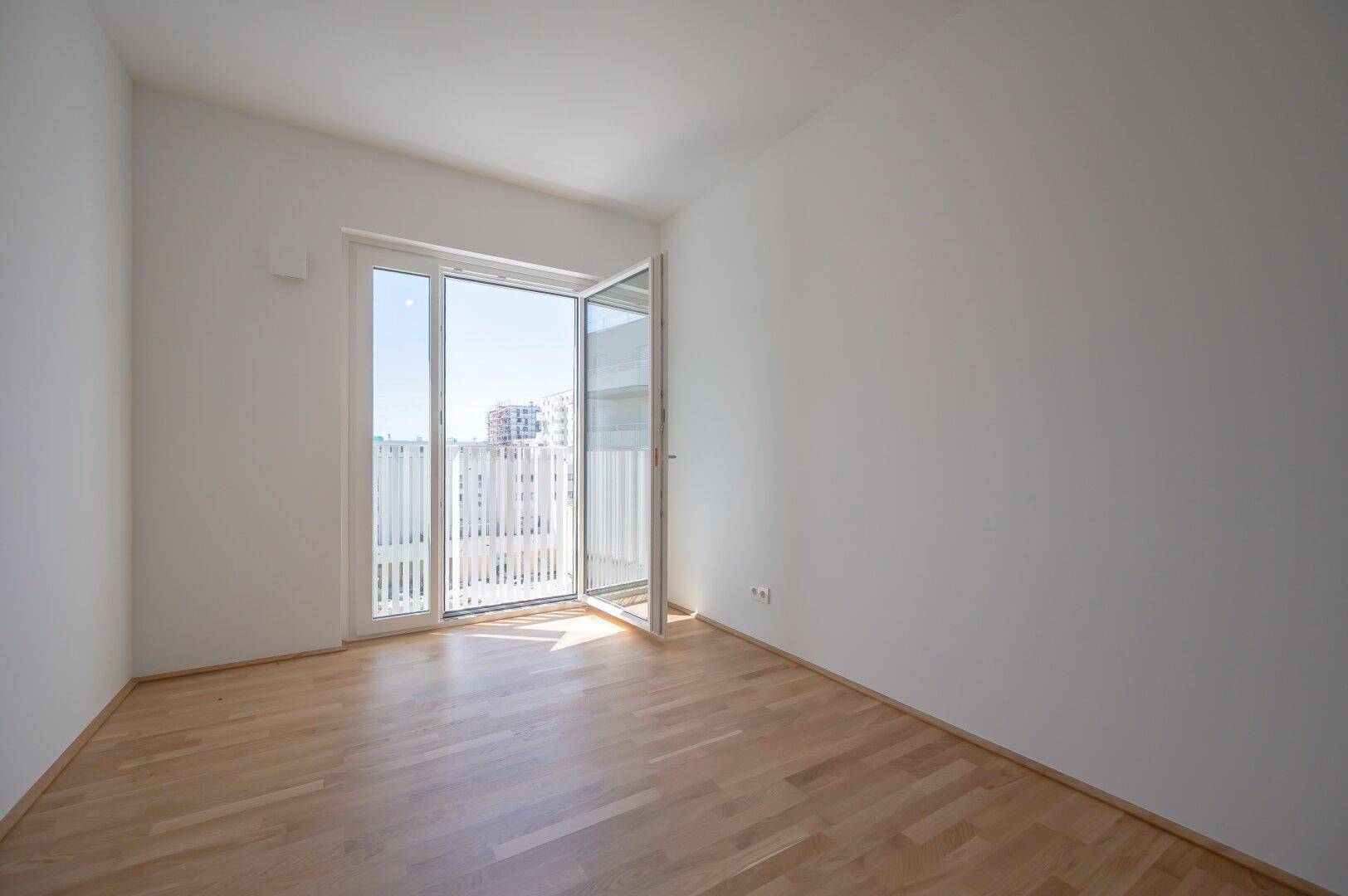 Leeres, helles Zimmer mit Parkettboden und Zugang zu einem Balkon, ideal als Schlaf- oder Arbeitszimmer.