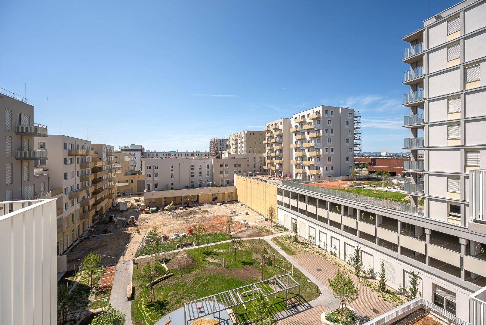 Weitläufiger Blick auf den begrünten Innenhof einer modernen Wohnanlage mit Spielplatz und Sitzgelegenheiten.