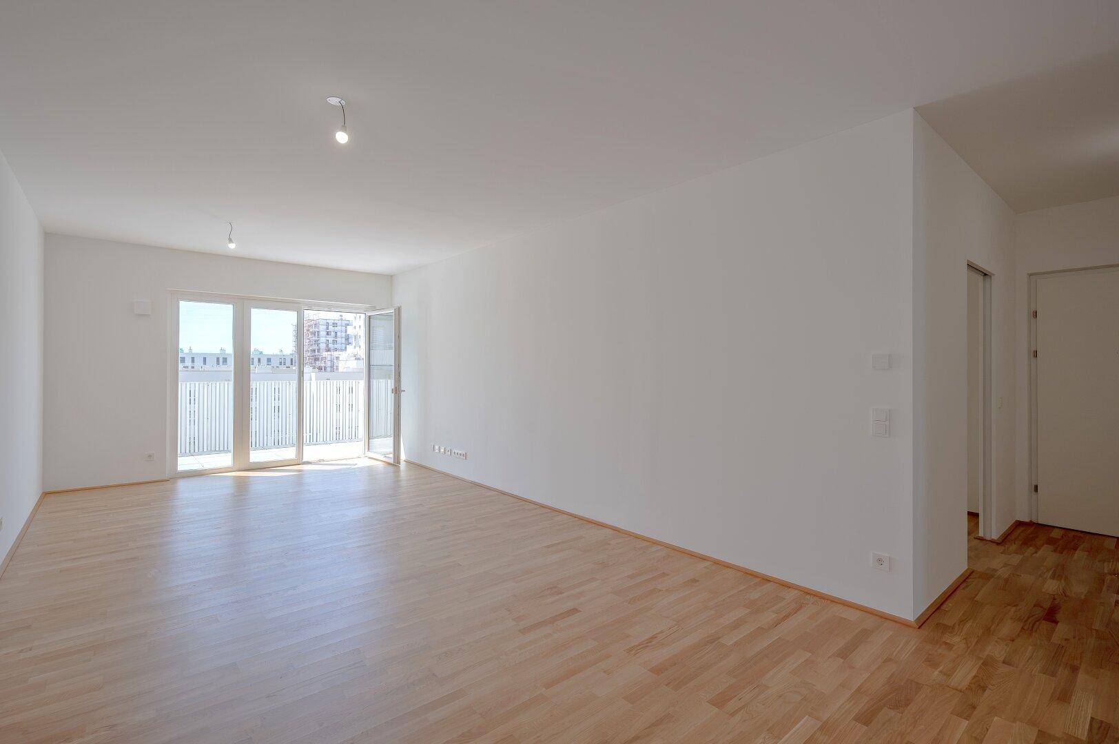 Geräumiges, lichtdurchflutetes Wohnzimmer mit hellem Parkettboden und breitem Zugang zu einem Außenbereich.