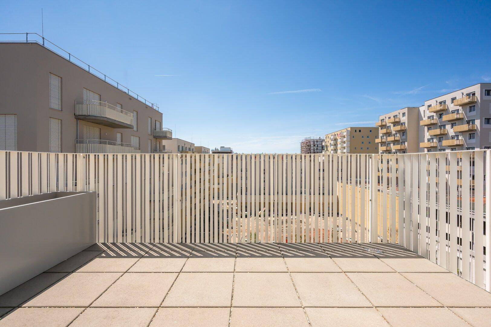 Große, sonnige Terrasse mit Fliesenboden und einer modernen Lamellenbrüstung, bietet viel Privatsphäre.