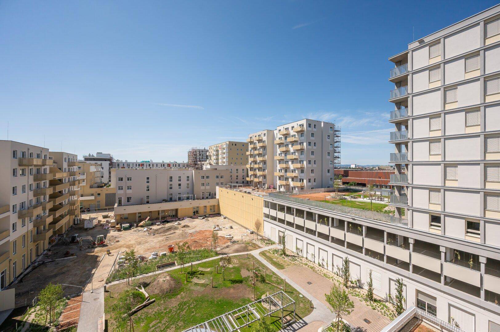 Panoramablick auf die moderne Wohnanlage mit Innenhof, Grünflächen und umliegenden Gebäuden.