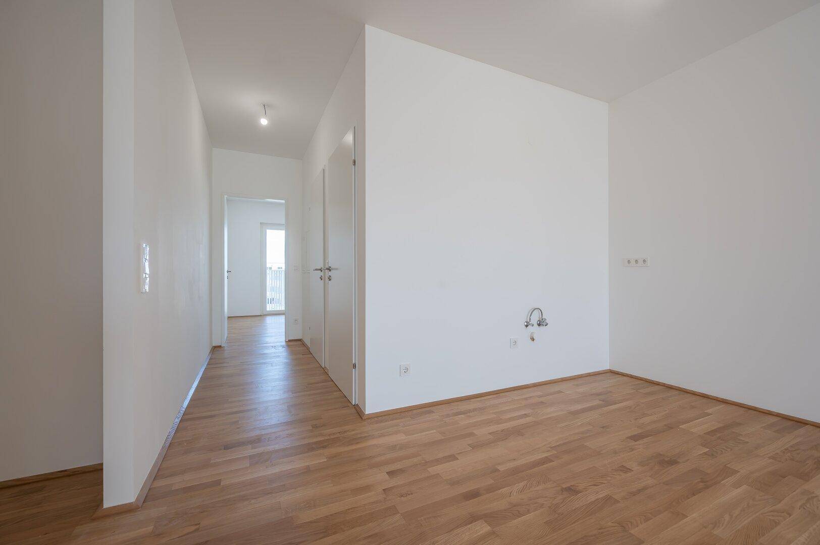 Helles Zimmer mit Parkettboden und Anschlüssen an der Wand, ideal für eine Küche oder Hauswirtschaftsraum.