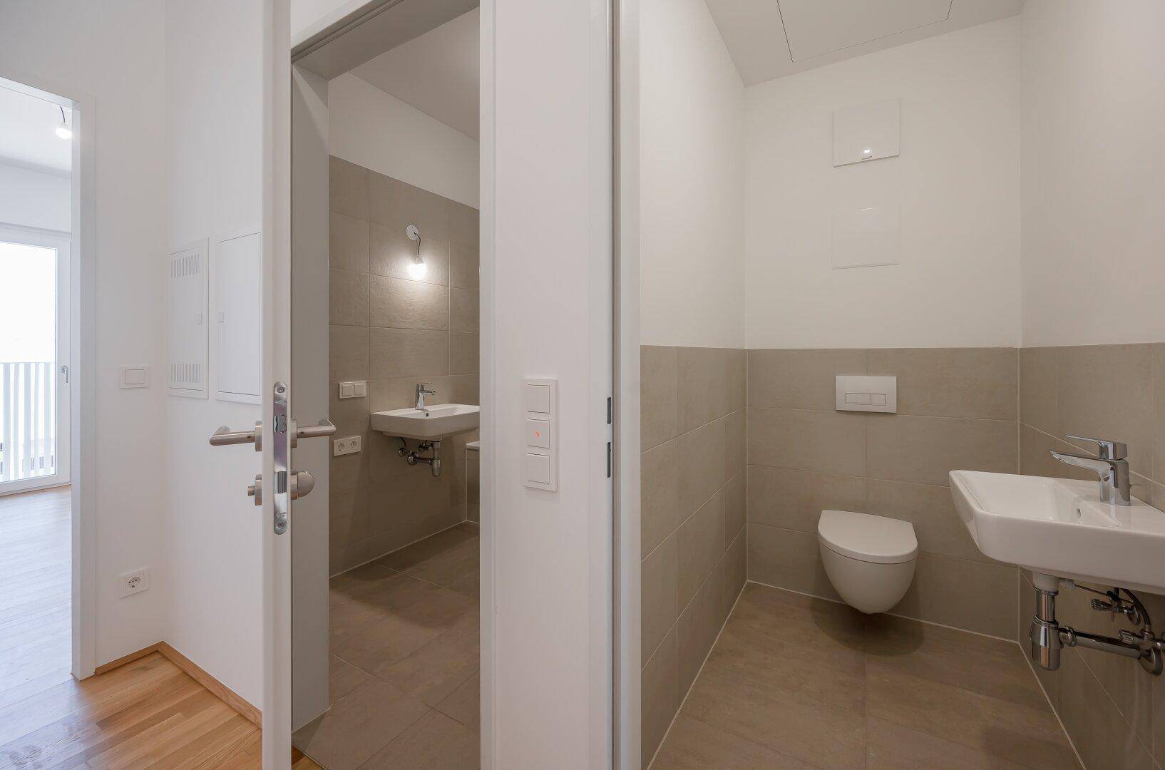 Modernes Gäste-WC mit Wand-WC und Waschbecken, angrenzend an ein weiteres Badezimmer.