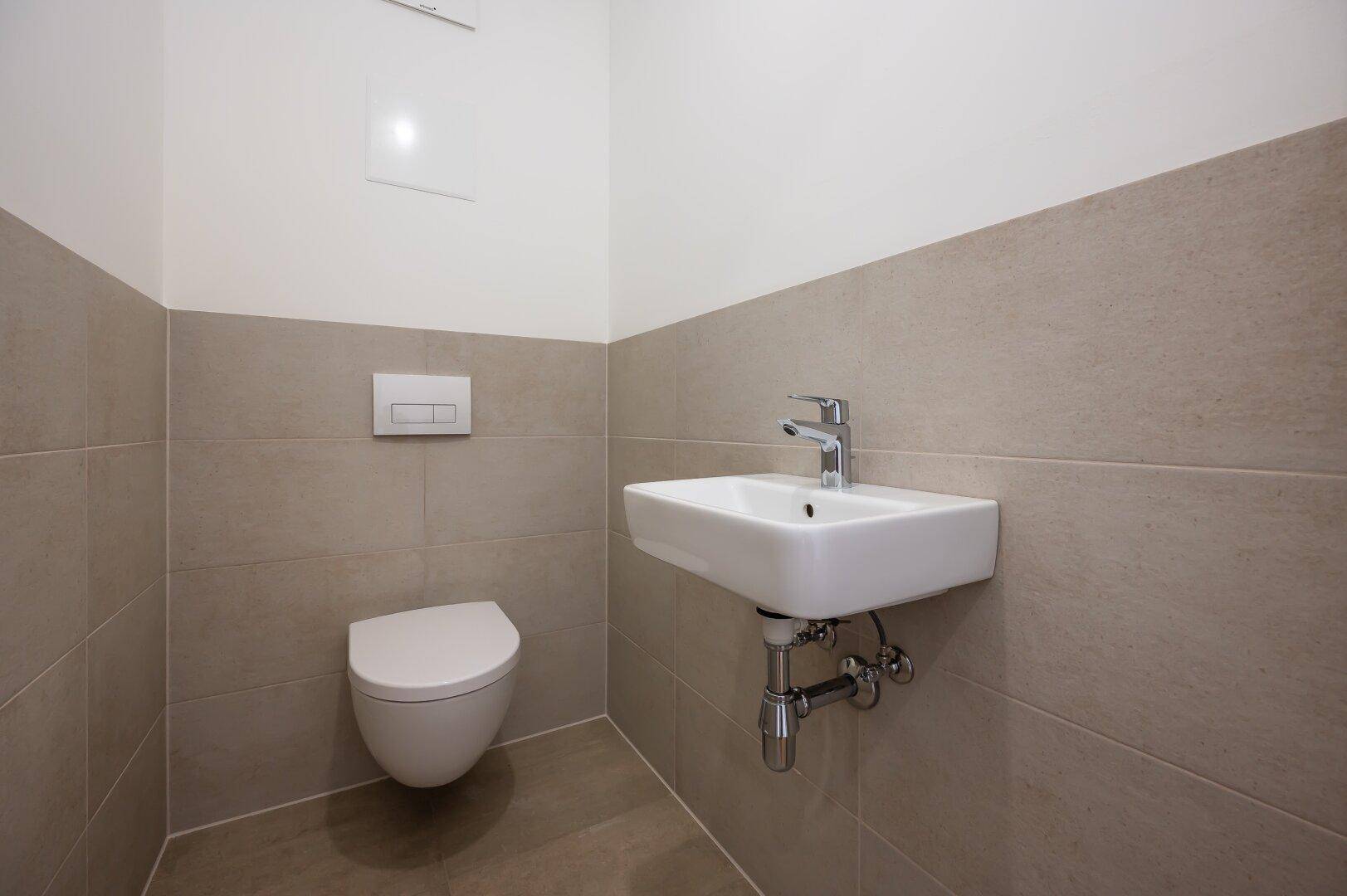 Funktionales Gäste-WC mit modernem Wand-WC und kleinem Waschbecken in neutralen Farben.