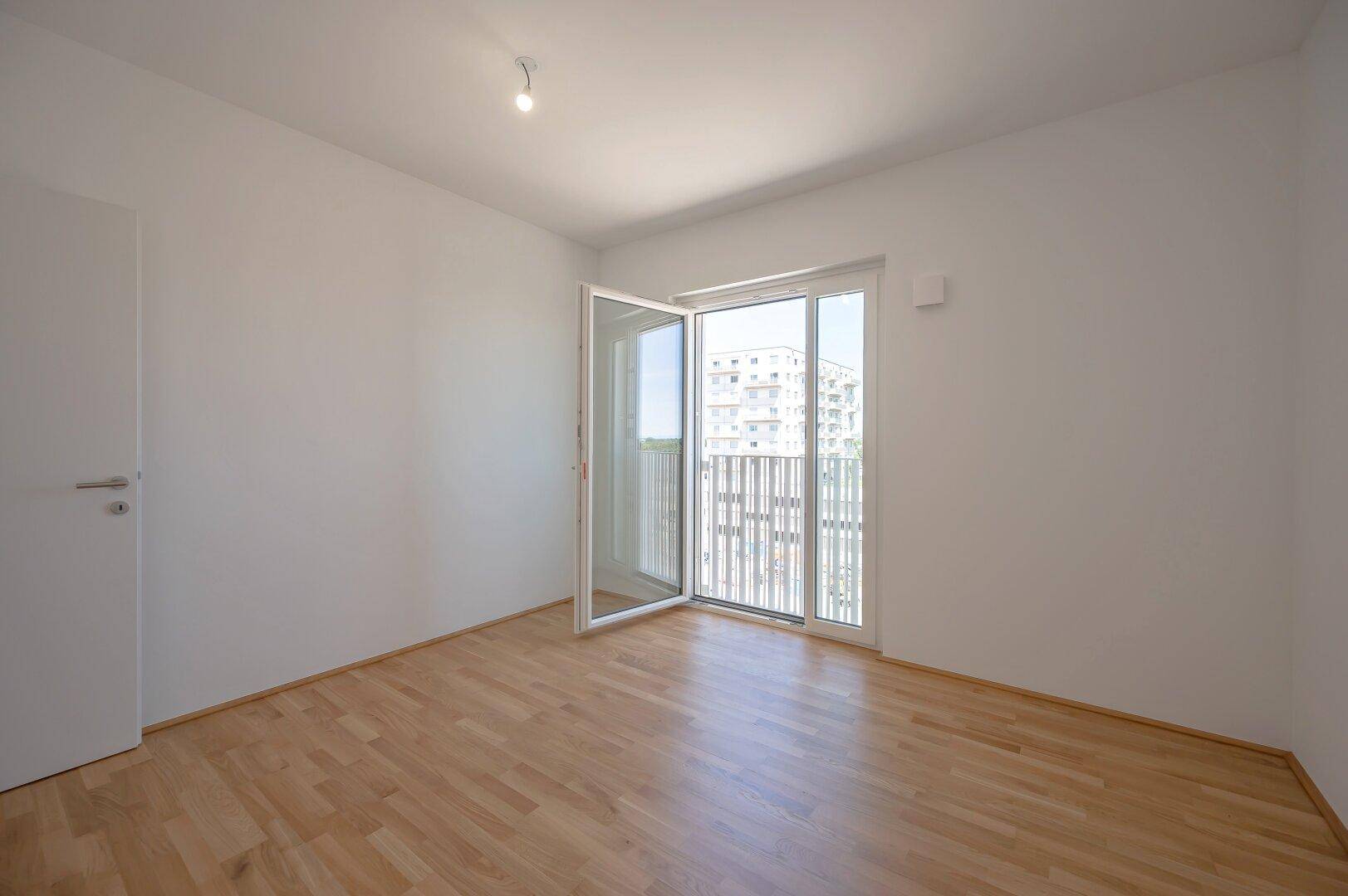 Helles Schlafzimmer mit Parkettboden und Zugang zu einem Balkon, bereit zur individuellen Einrichtung.