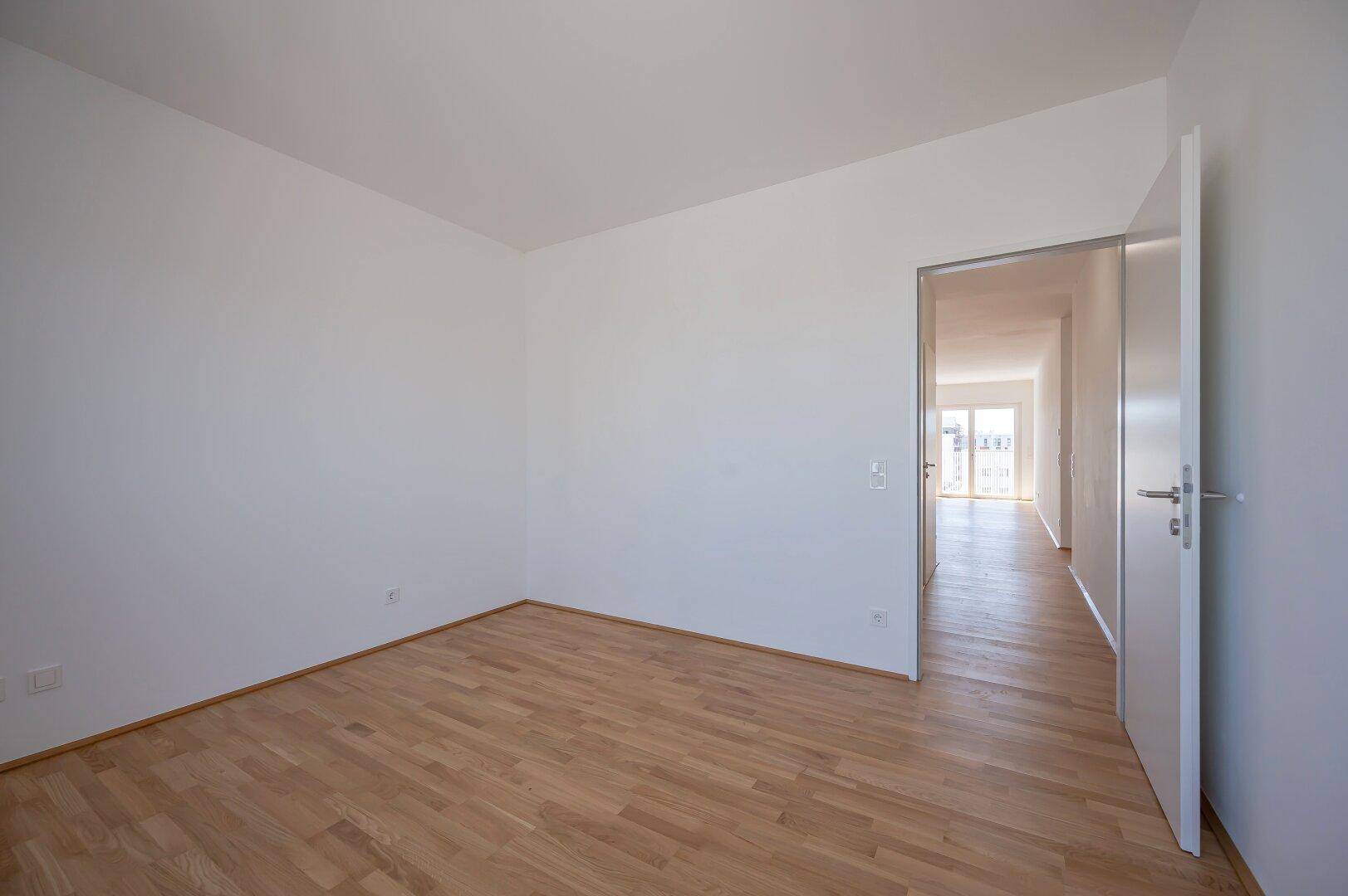 Leeres Zimmer mit Parkettboden und weiß gestrichenen Wänden, ideal als Schlaf- oder Kinderzimmer.