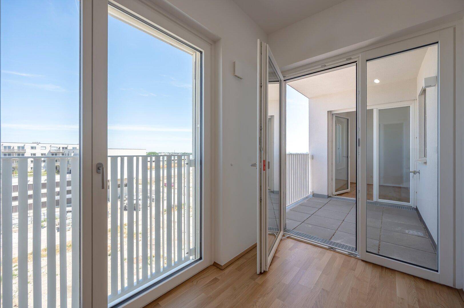 Große Fensterfronten im Wohnbereich bieten Zugang zum Balkon und viel Tageslicht.
