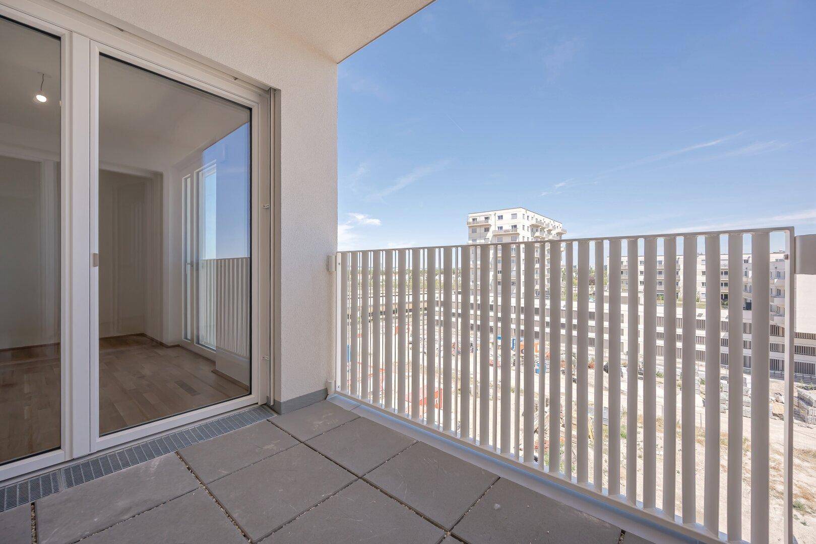 Geräumiger Balkon mit Fliesenboden und Blick auf die umliegende Neubausiedlung.