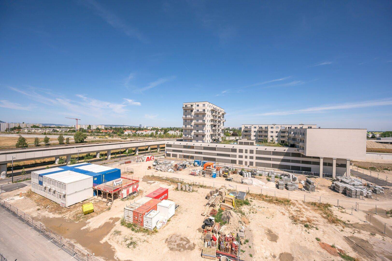 Weitläufige Baustelle mit Blick auf ein modernes Wohngebäude unter blauem Himmel.