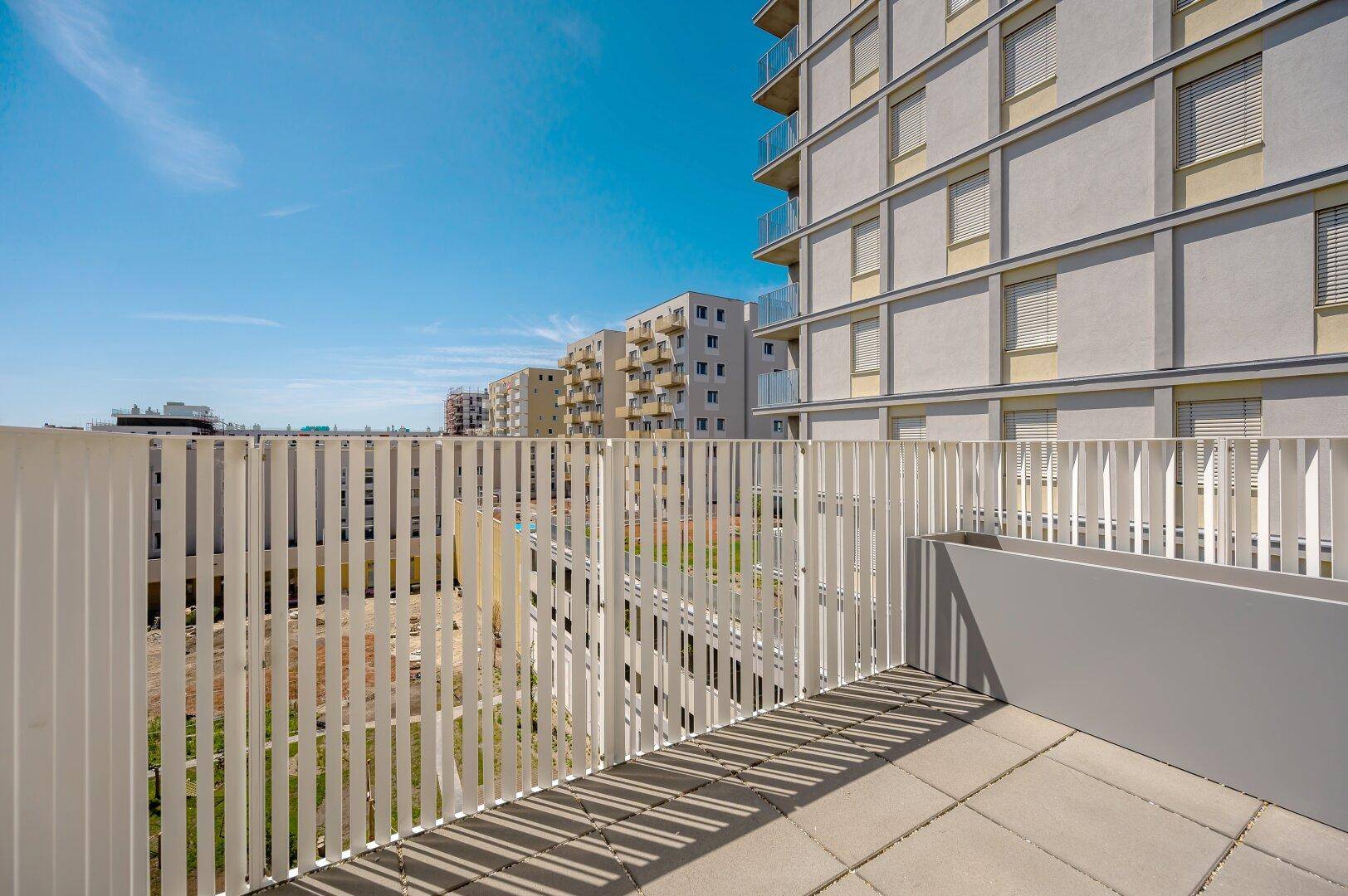 Blick von einem modernen Balkon mit weißem Geländer auf die umliegenden Neubauten.
