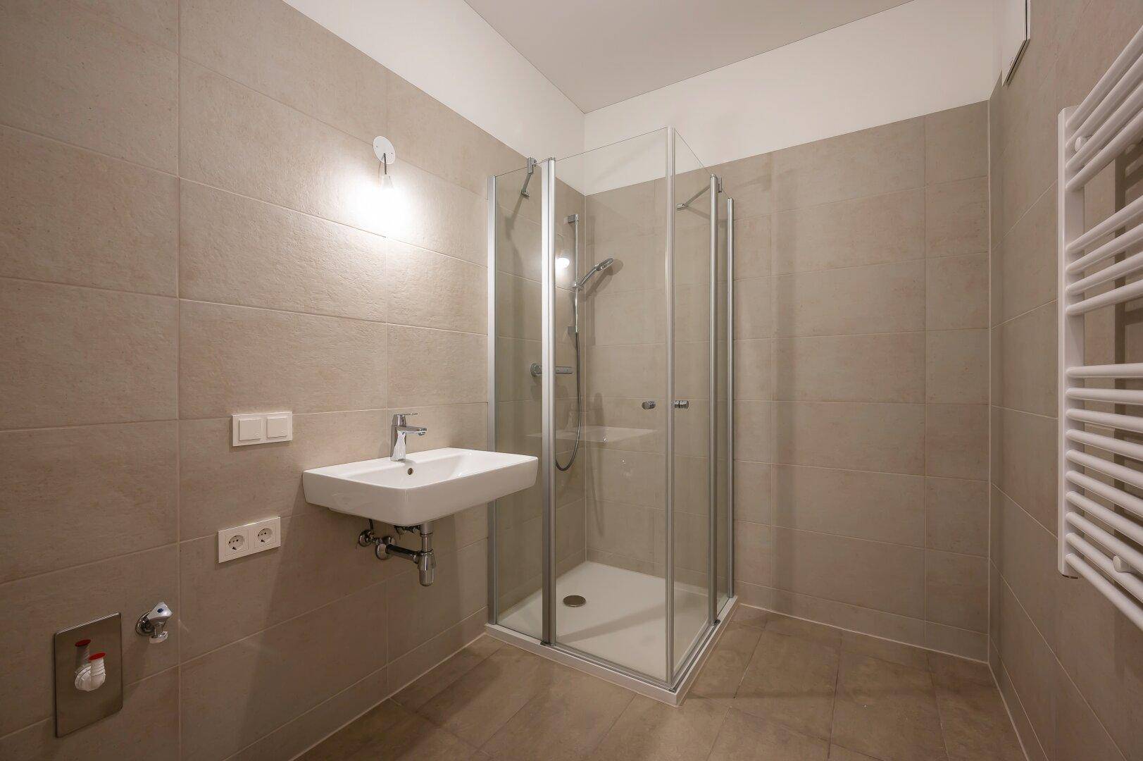 Modernes Badezimmer mit Duschkabine, Waschbecken und beheiztem Handtuchhalter.