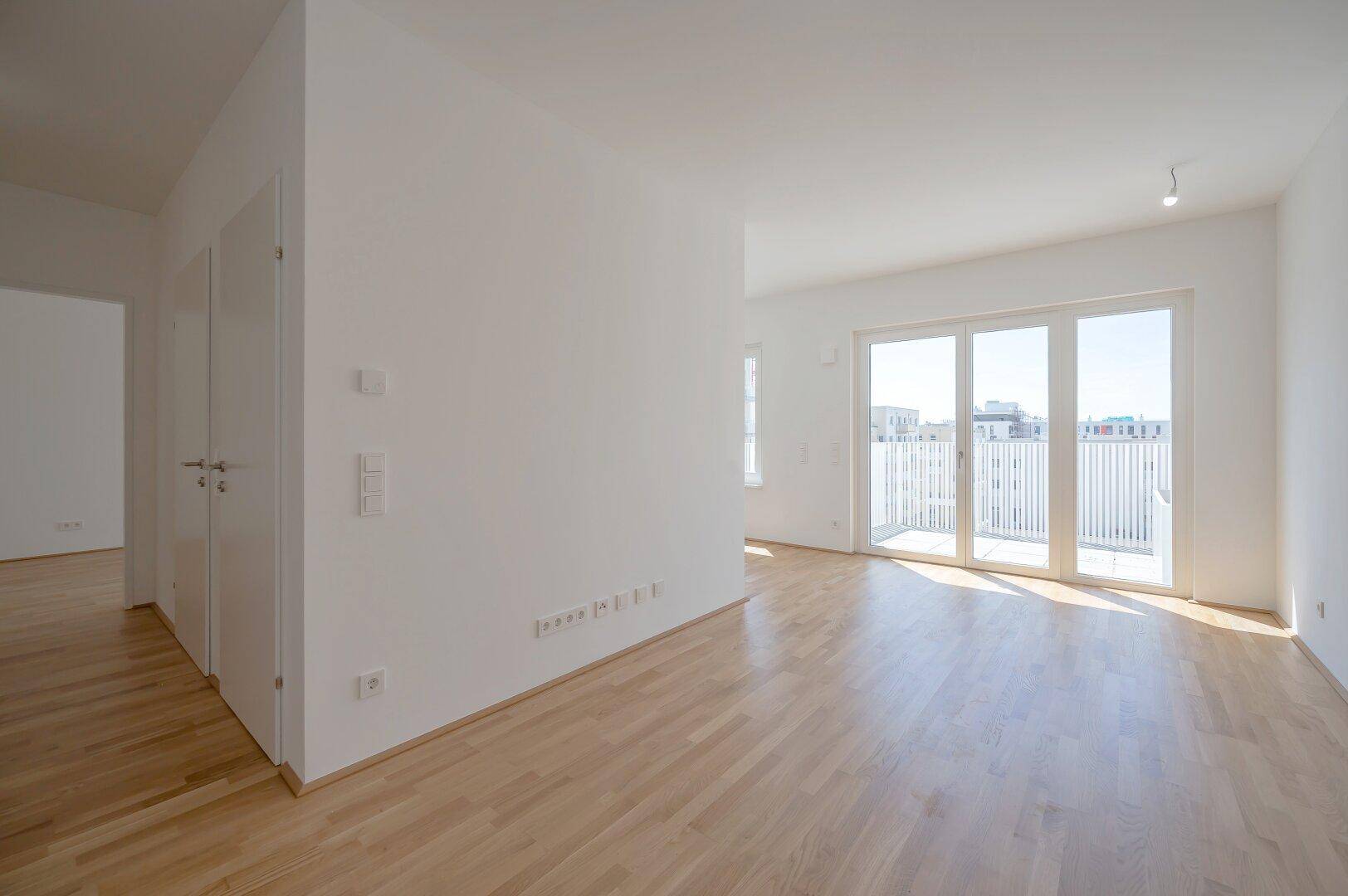 Großzügiger, heller Wohnbereich mit Holzboden und Zugang zu einem Balkon.