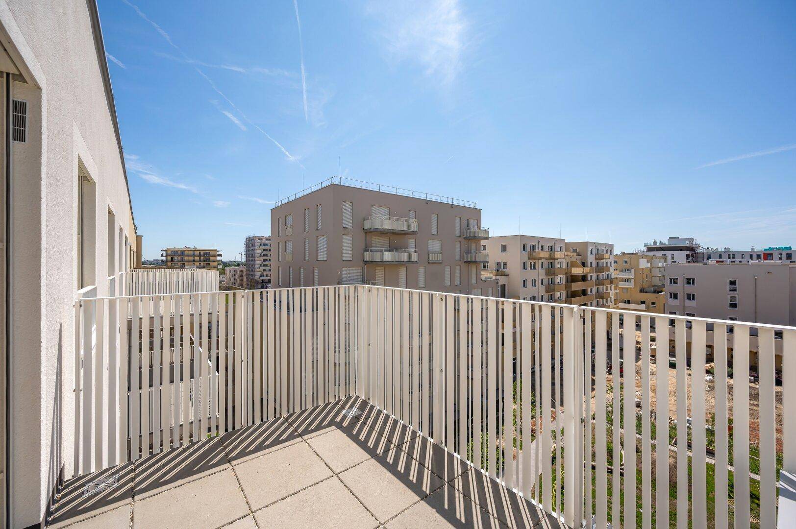 Sonniger Balkon mit weißem Geländer und Ausblick auf die umliegenden Neubauten.