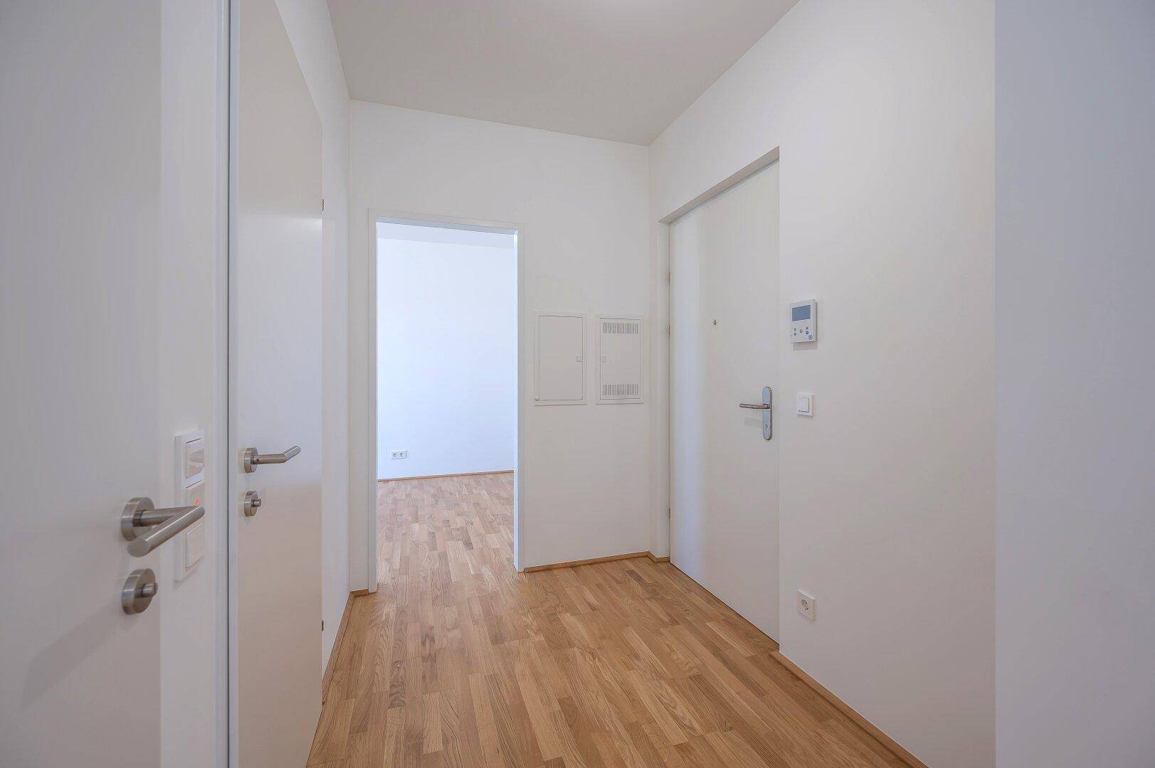 Heller Flur mit Holzboden und weißen Türen, der zu weiteren Räumen der Wohnung führt.