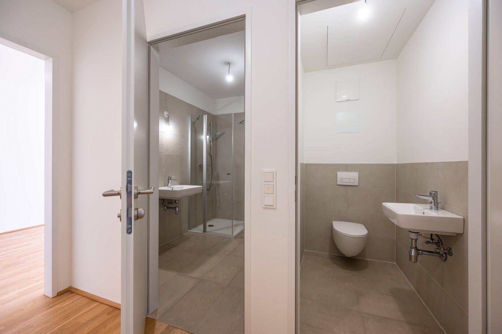 Moderner Badezimmer- und WC-Bereich mit hellen Fliesen und Dusche.