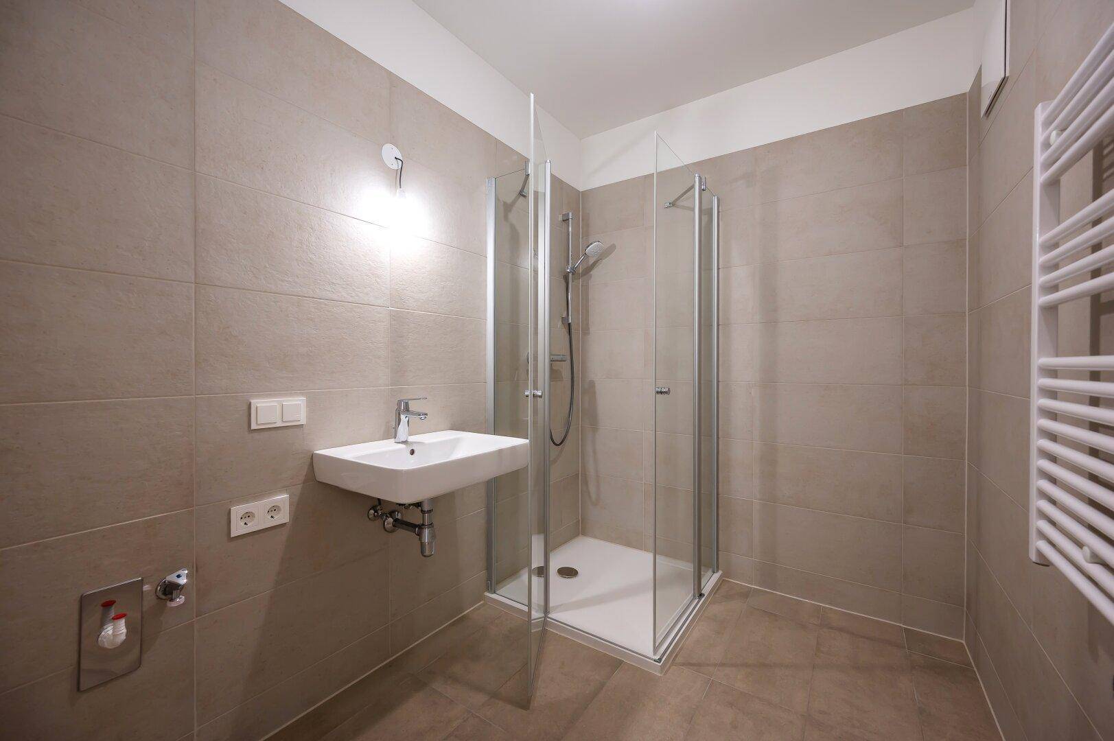 Modernes Badezimmer mit Duschkabine, Waschbecken und Handtuchheizkörper.