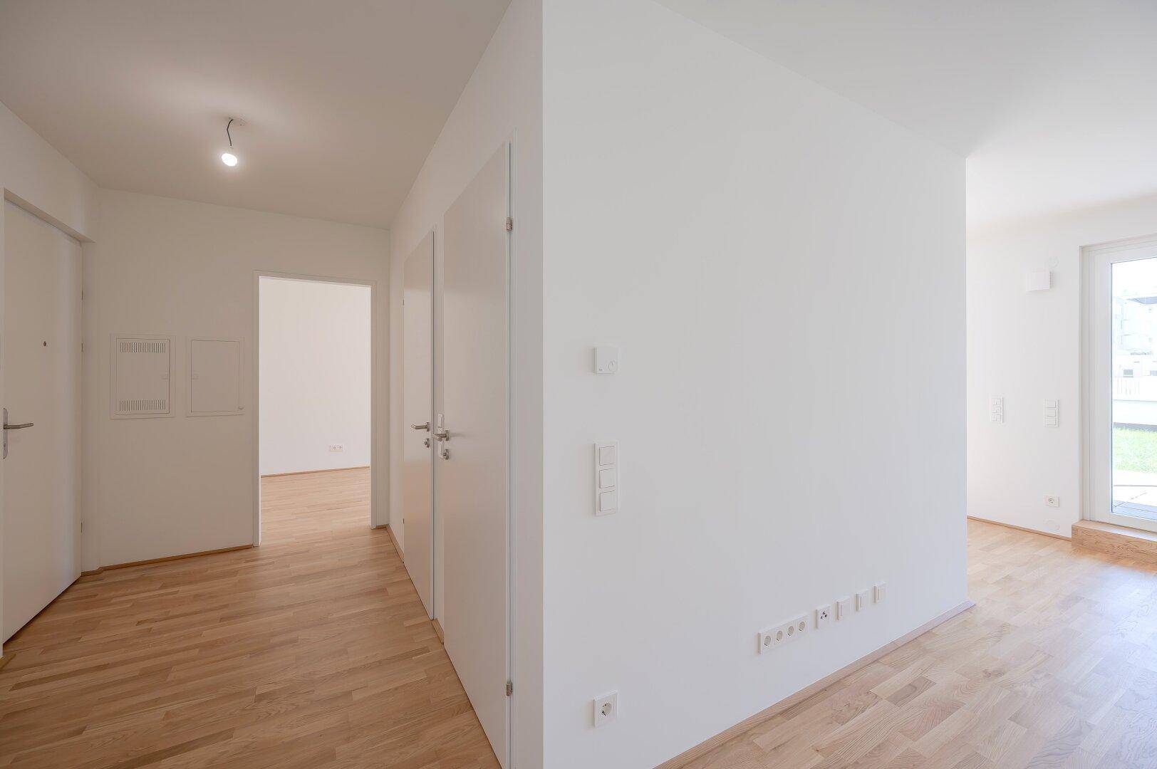 Heller Flur mit Holzboden und weißen Türen in einem Neubau.