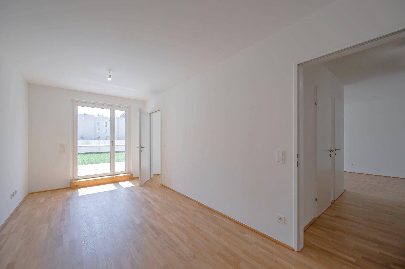 Heller Raum mit Holzboden und großem Fenster mit Blick ins Grüne.