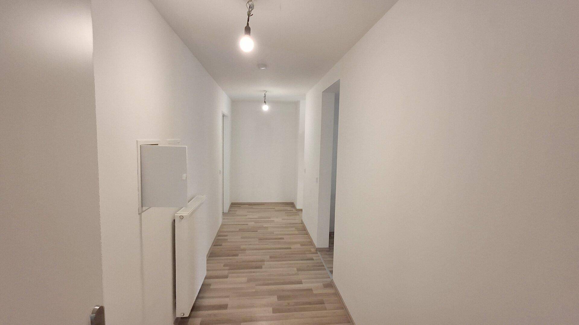 Heller Flur mit modernem Laminatboden und weißen Wänden, der zu weiteren Räumen führt.