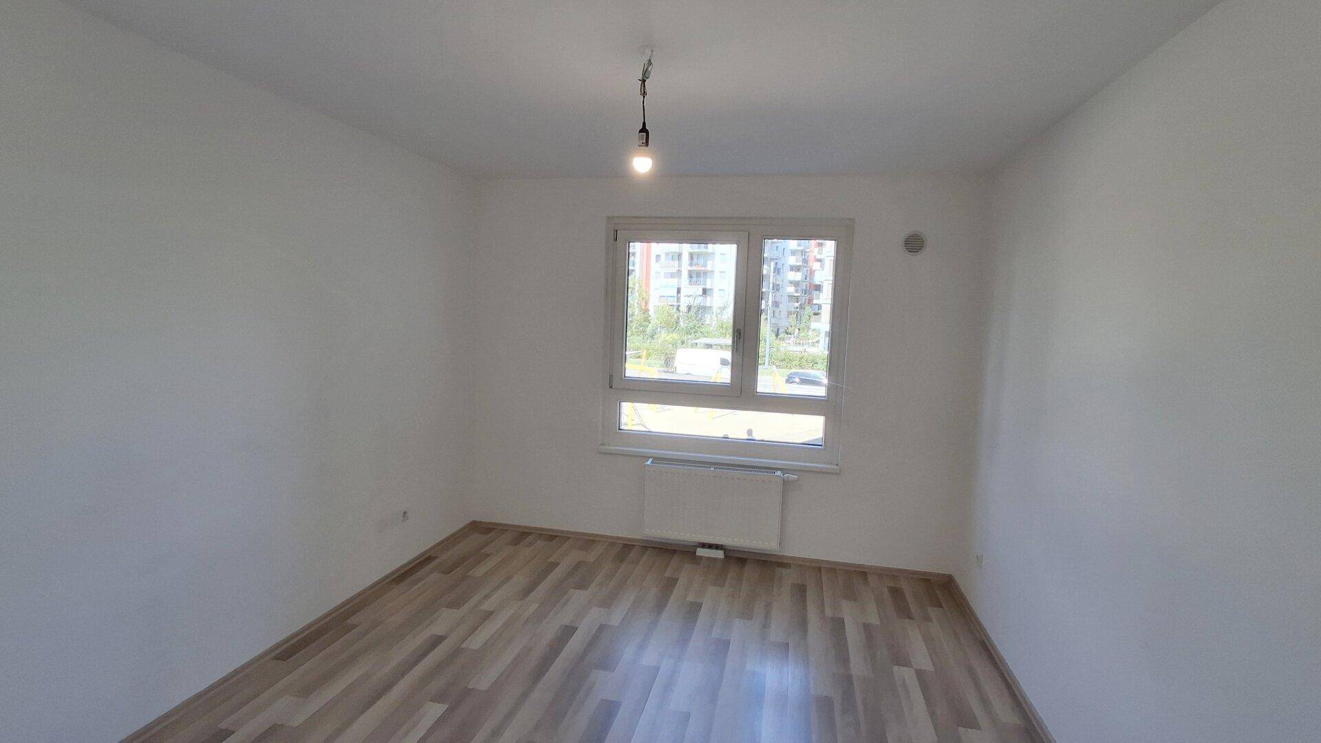 Geräumiges Schlafzimmer mit Laminatboden, weißen Wänden und einem großen Fenster.