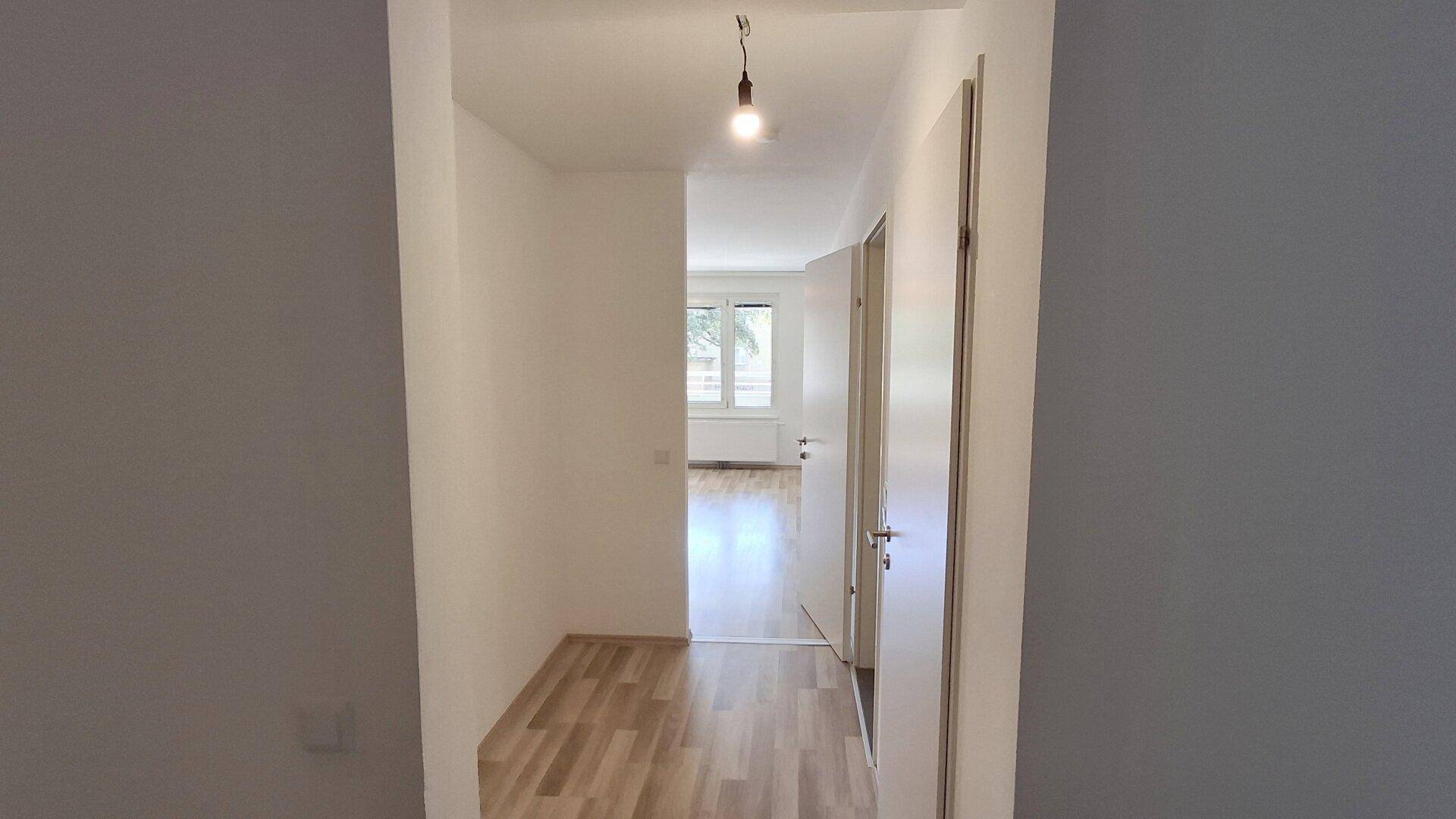 Blick vom Flur in einen weiteren Raum mit hellem Laminatboden und weißen Türen.