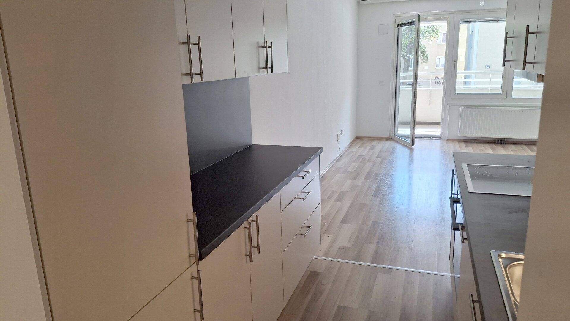 Blick von der Küche in den Wohnbereich mit Balkonzugang und hellem Laminatboden.