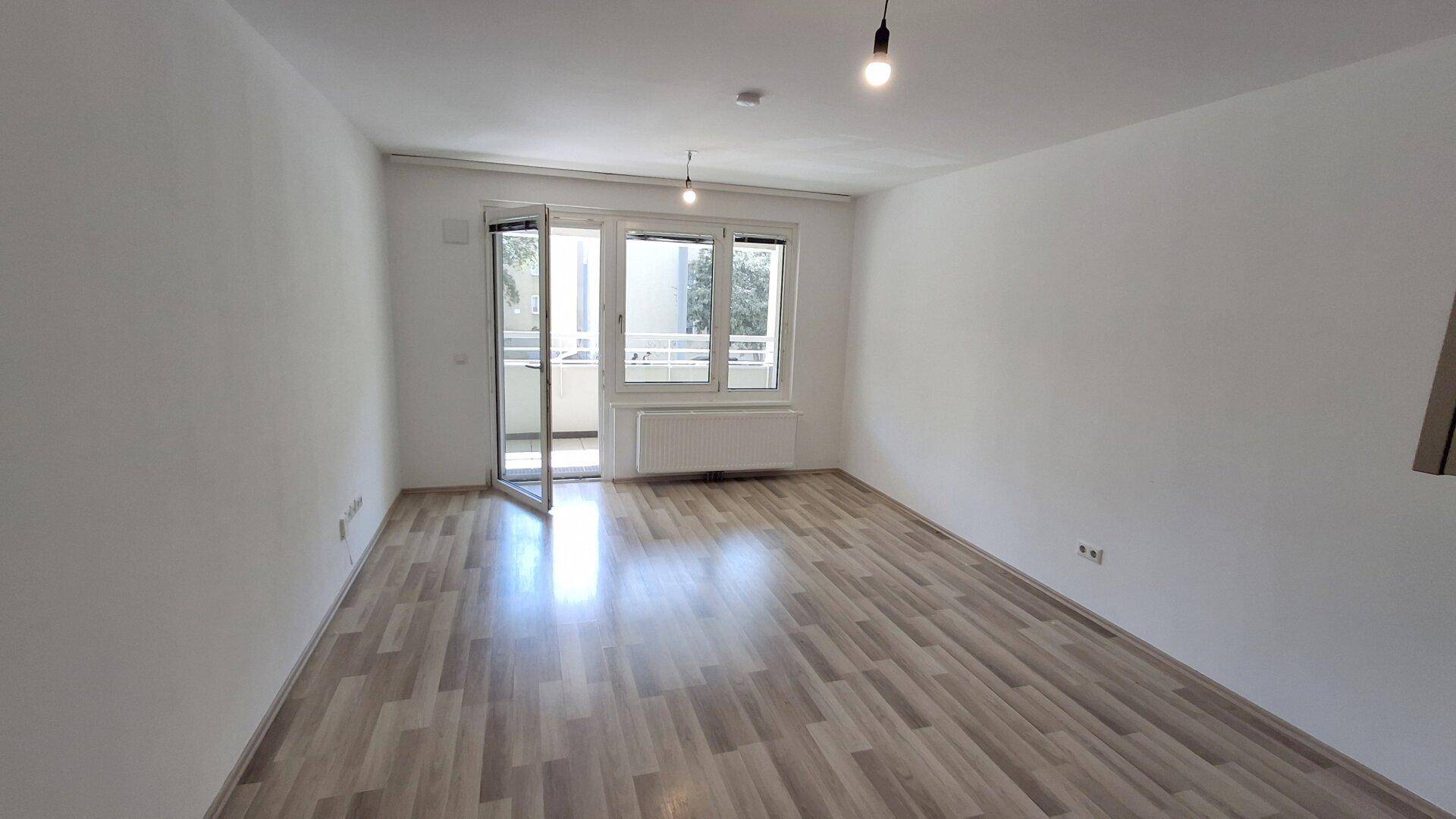 Geräumiges Wohnzimmer mit Laminatboden, weißen Wänden und direktem Zugang zum Balkon.