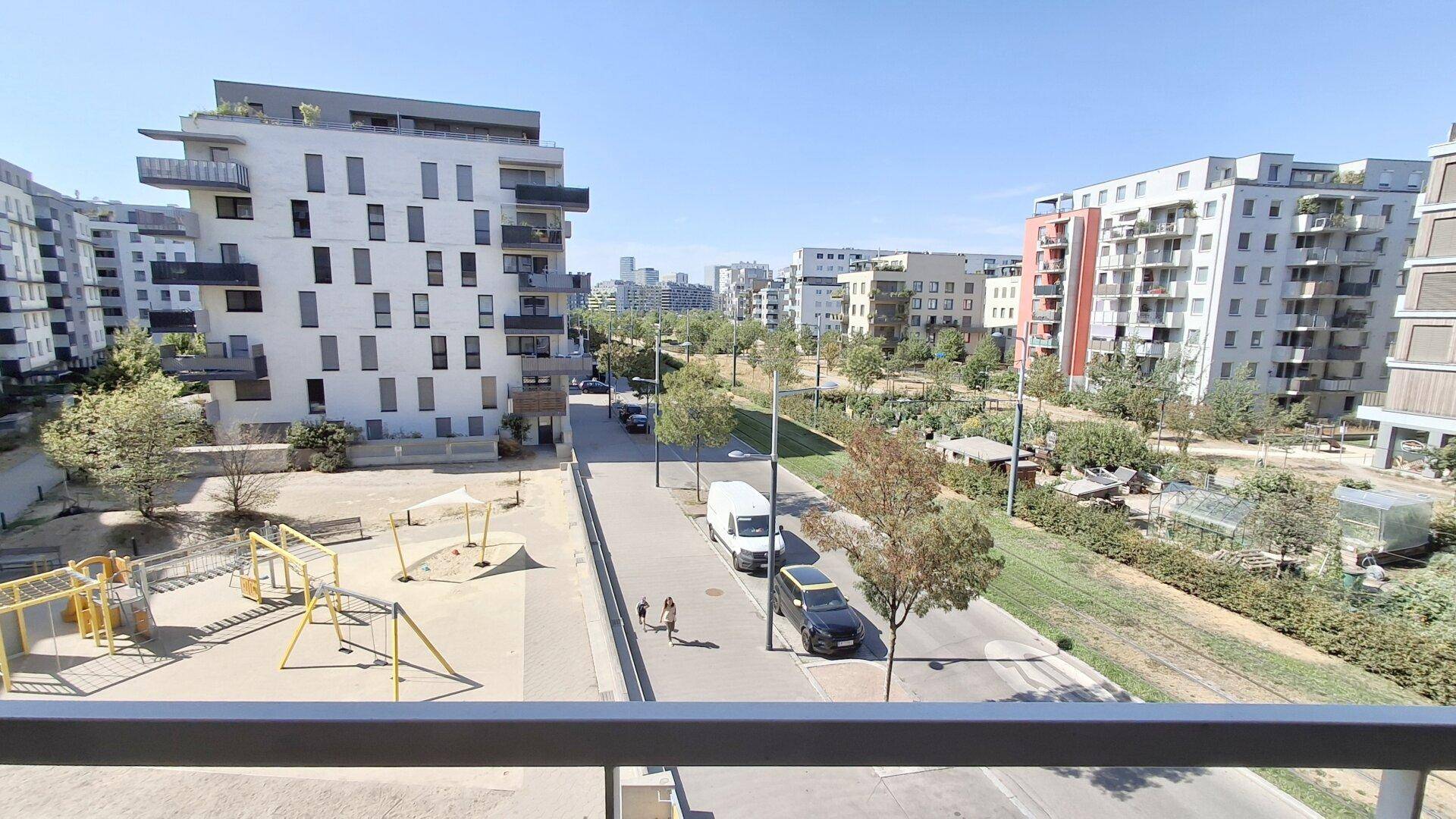 Weitläufiger Blick vom Balkon auf einen Spielplatz, die Straße und moderne Wohngebäude.