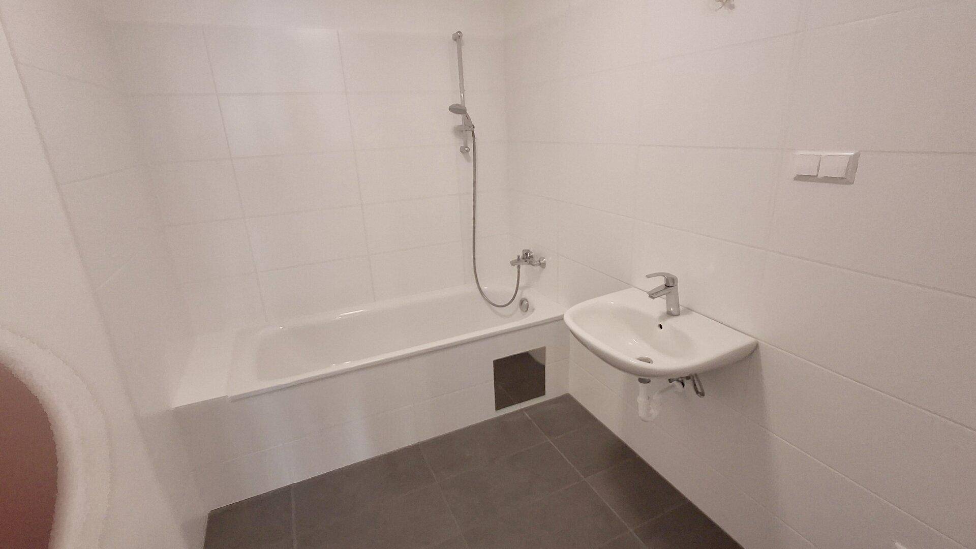 Modernes Badezimmer mit Badewanne, integrierter Dusche und weiß gefliesten Wänden und dunklem Boden.
