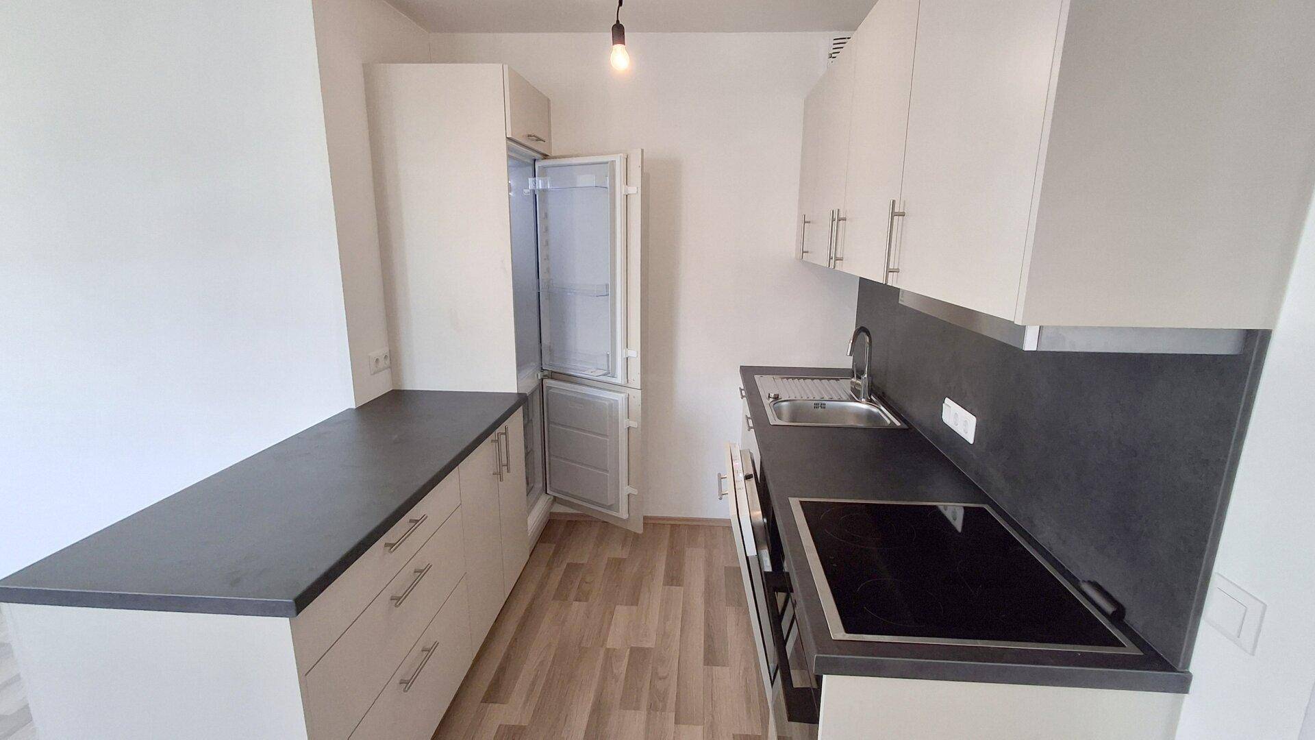 Moderne Einbauküche mit Kühlschrank, weißen Schränken und dunkler Arbeitsplatte, gut ausgestattet.