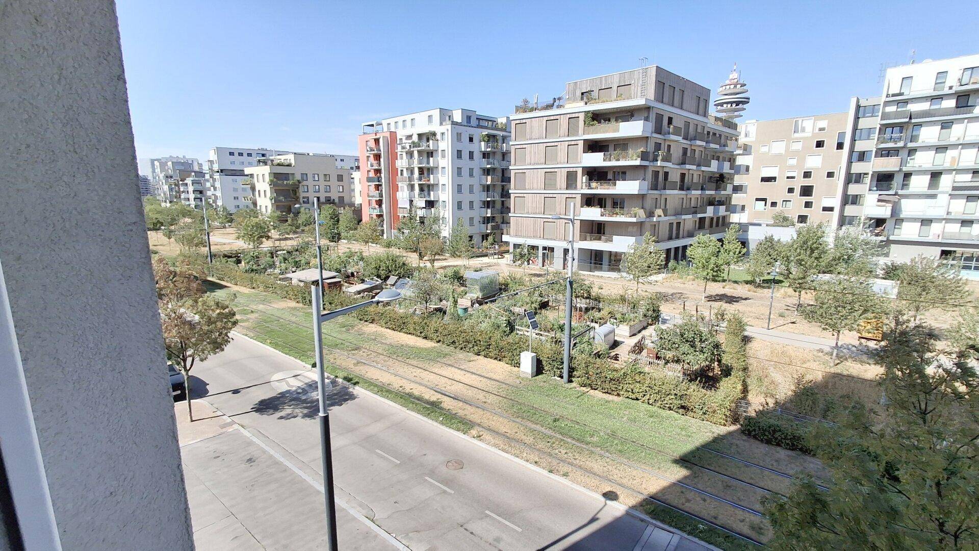 Weitläufiger Blick auf moderne Wohngebäude, Grünflächen und eine Straße mit Tramgleisen.